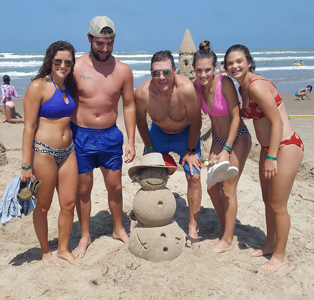 A family of 5 adults standing on South Padre island beach behind a 3ft snowman made from sand using the sand shaper tool and the science of sandcastle building system