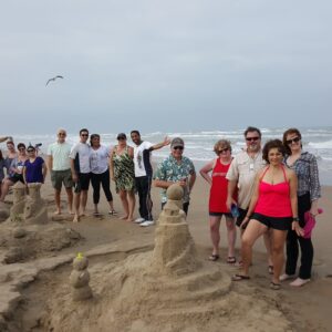 30 people enjoying a Corporate Team Building class standing next to their team sandcastles on south padre island beach after a lesson in building BIG Sandcastles with American Champion Andy Hancock