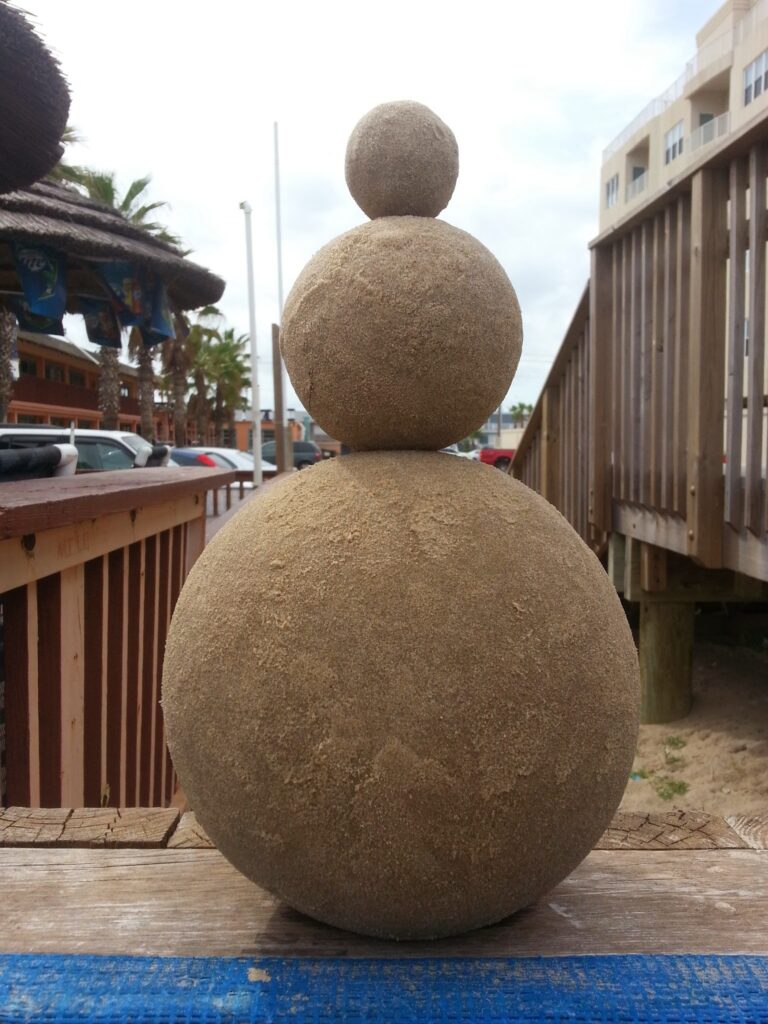 A stack of 3 solid sand spheres - 8 inch at the base with 3 and 2 inch balls above, all balancing on top of one another, made by Andy Hancock on South Padre Island to show how to test the geology of your beach sand to build successful sandcastles worldwide using science and professional tools